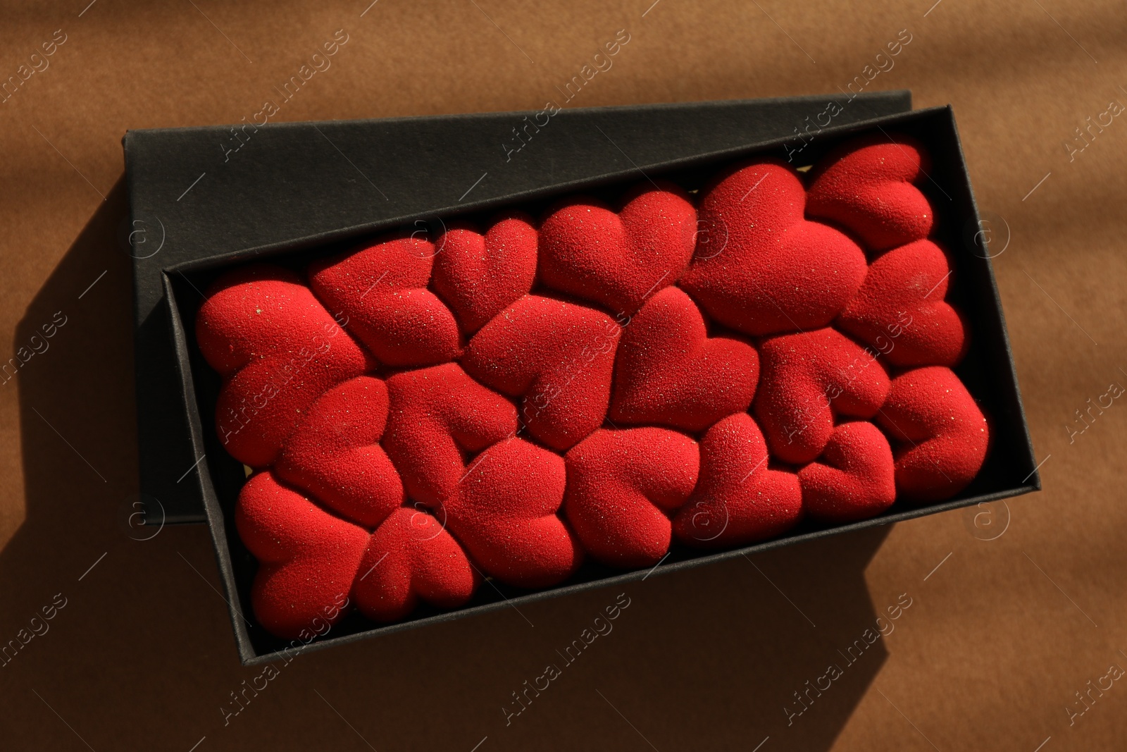 Photo of Chocolate bar decorated with hearts on brown background, top view