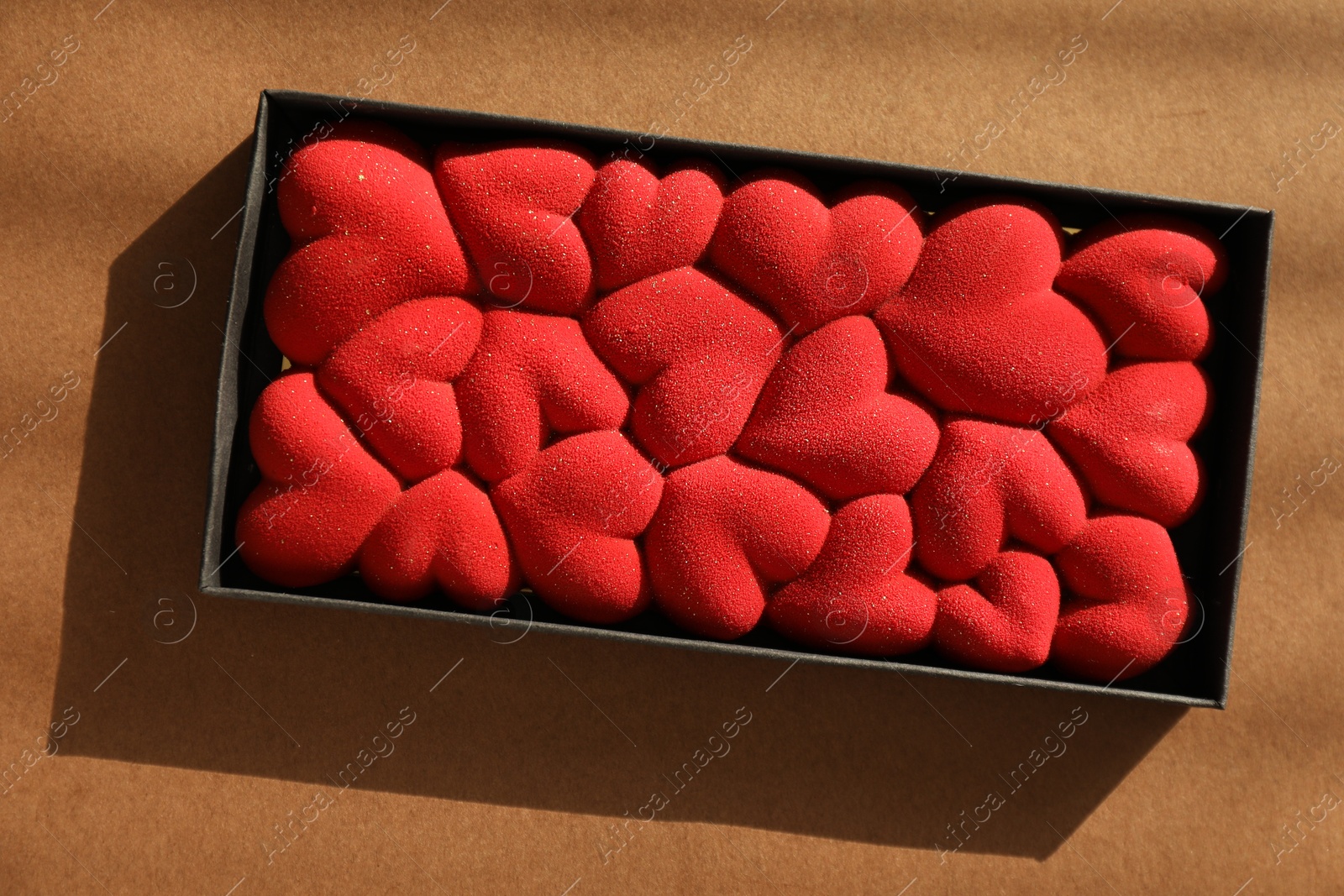 Photo of Chocolate bar decorated with hearts on brown background, top view