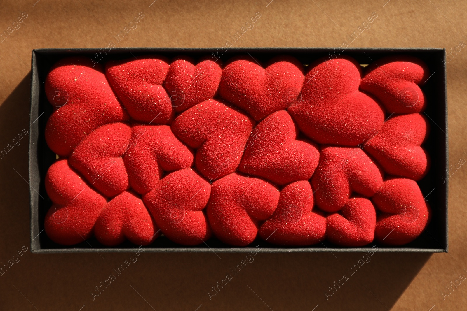 Photo of Chocolate bar decorated with hearts on brown background, top view