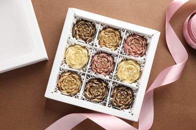 Photo of Delicious flower shaped chocolate bonbons in box on brown background, flat lay