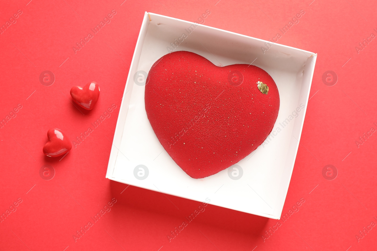 Photo of Heart shaped chocolate in box and candies on red background, top view