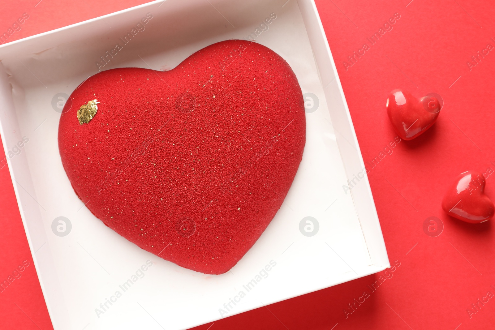 Photo of Heart shaped chocolate in box and candies on red background, top view