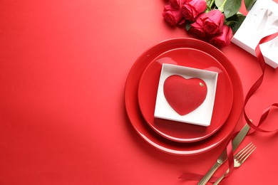 Photo of Heart shaped chocolate in box on plate and roses against red background, flat lay. Space for text