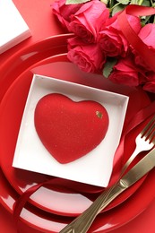 Photo of Heart shaped chocolate in box on plate and roses against red background, flat lay