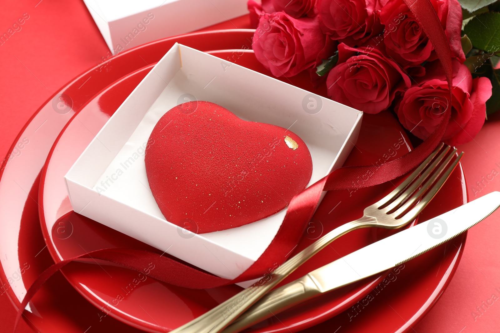 Photo of Heart shaped chocolate in box on plate and roses against red background, closeup