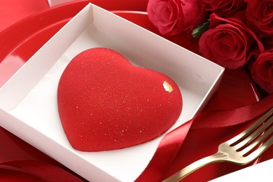 Photo of Heart shaped chocolate in box on plate and roses against red background, closeup