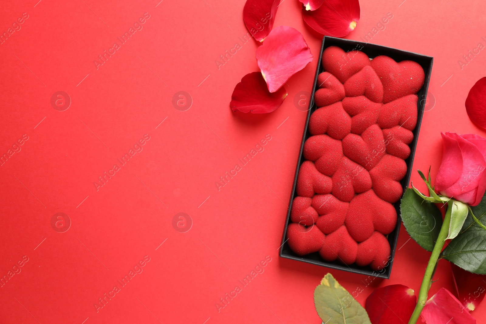 Photo of Chocolate bar decorated with hearts, rose and petals on red background, flat lay. Space for text