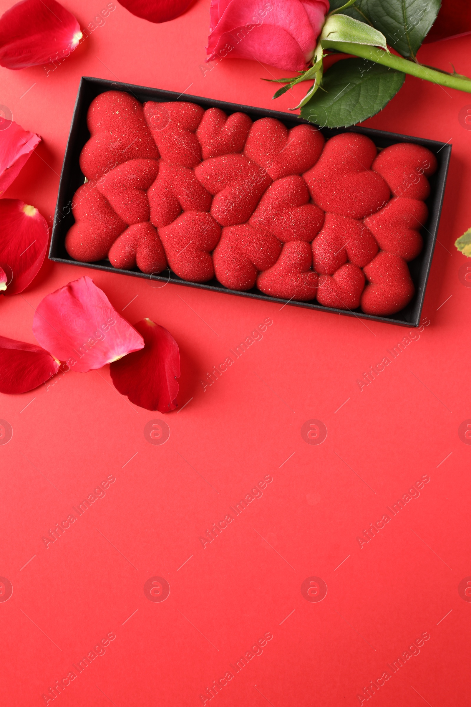 Photo of Chocolate bar decorated with hearts, rose and petals on red background, flat lay. Space for text