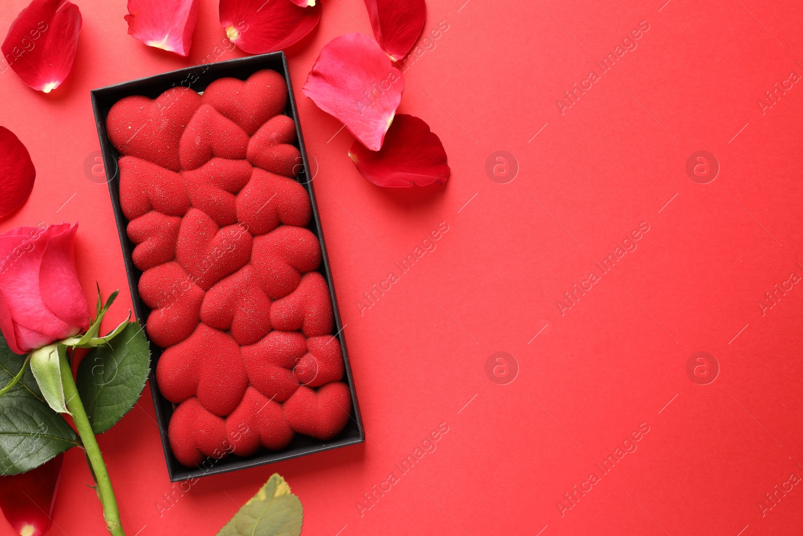 Photo of Chocolate bar decorated with hearts, rose and petals on red background, flat lay. Space for text