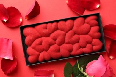 Photo of Chocolate bar decorated with hearts, rose and petals on red background, flat lay