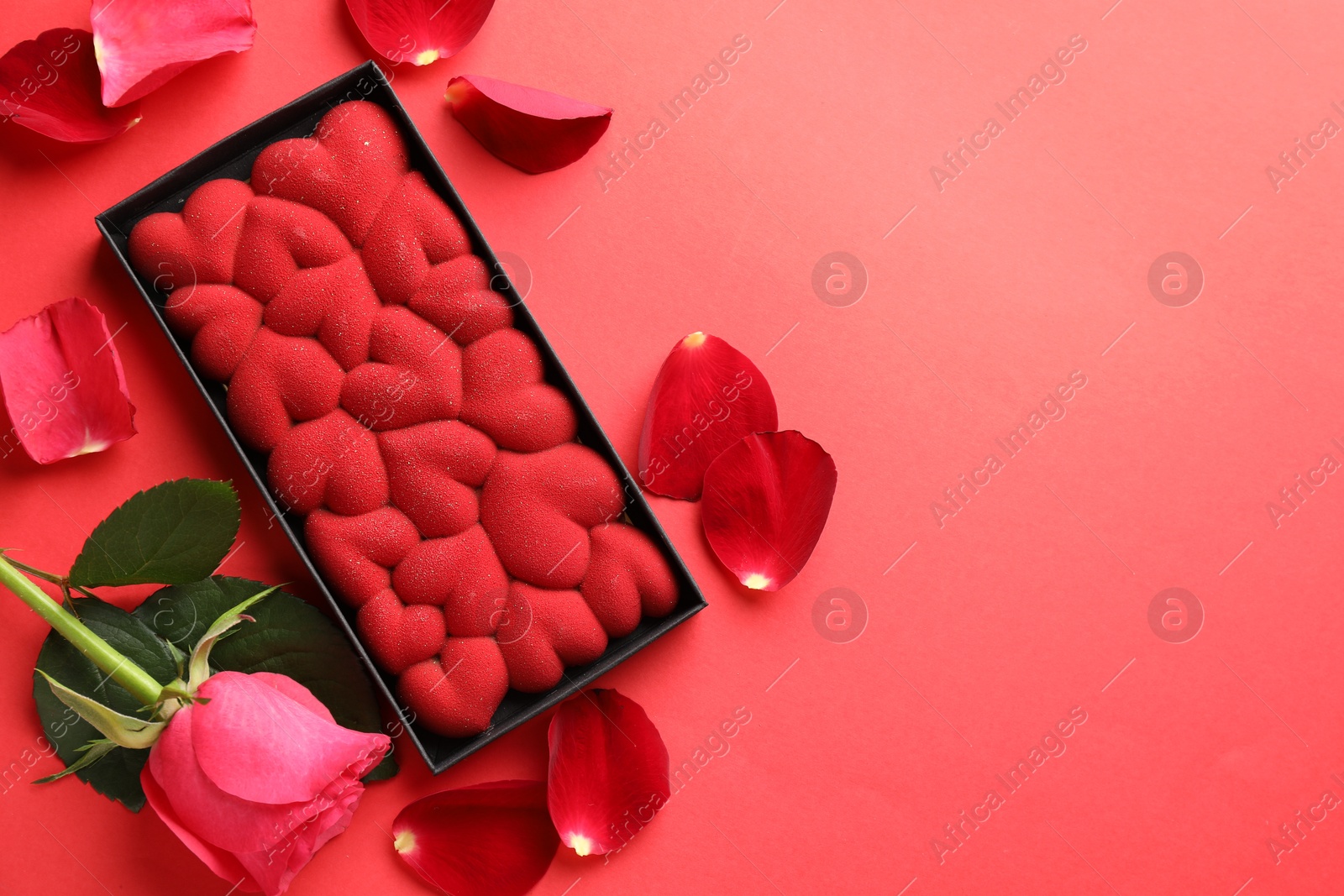 Photo of Chocolate bar decorated with hearts, rose and petals on red background, flat lay. Space for text