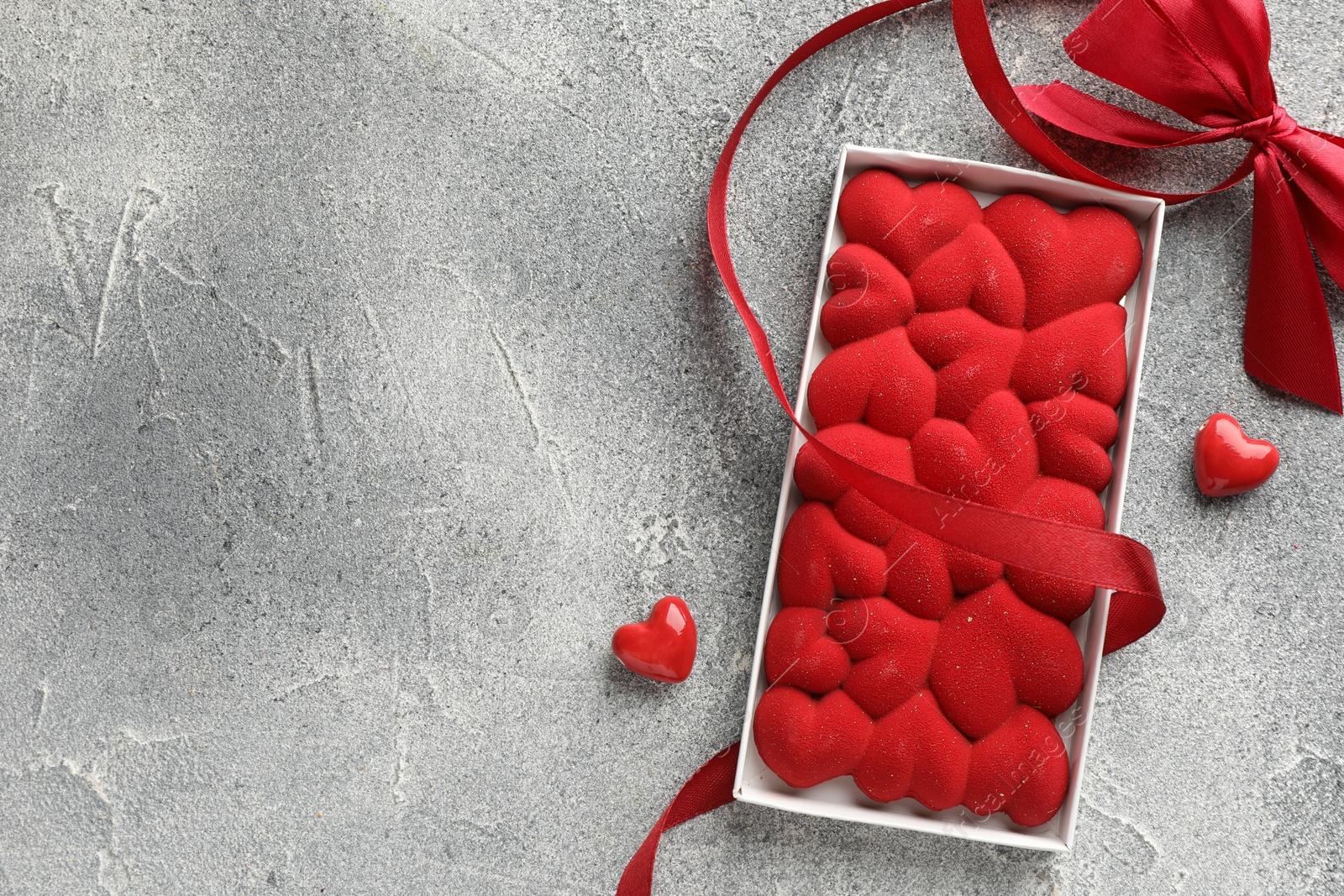 Photo of Chocolate bar decorated with hearts, candies and ribbon on grey textured background, top view. Space for text