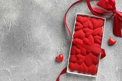 Photo of Chocolate bar decorated with hearts, candies and ribbon on grey textured background, top view. Space for text