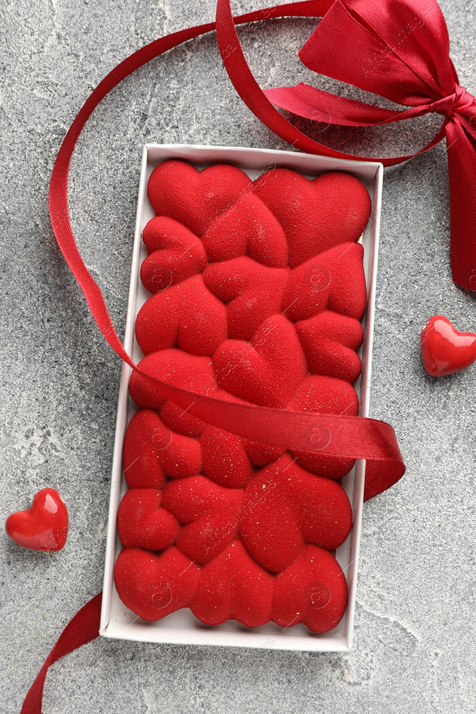 Photo of Chocolate bar decorated with hearts, candies and ribbon on grey textured background, top view