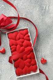 Photo of Chocolate bar decorated with hearts, candies and ribbon on grey textured background, top view