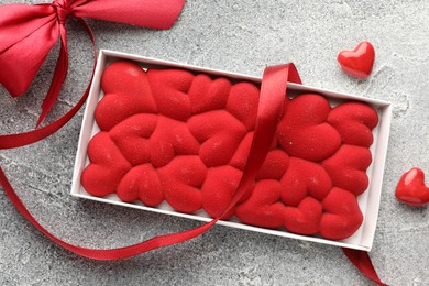 Photo of Chocolate bar decorated with hearts, candies and ribbon on grey textured background, top view