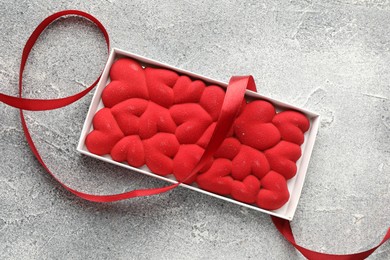 Photo of Chocolate bar decorated with hearts and ribbon on grey textured background, top view