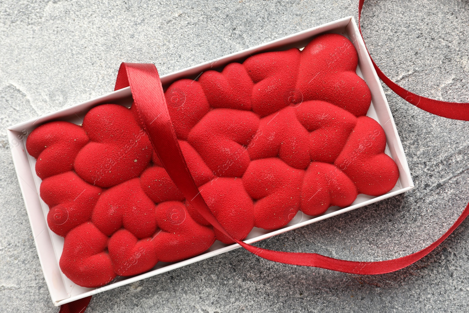 Photo of Chocolate bar decorated with hearts and ribbon on grey textured background, top view