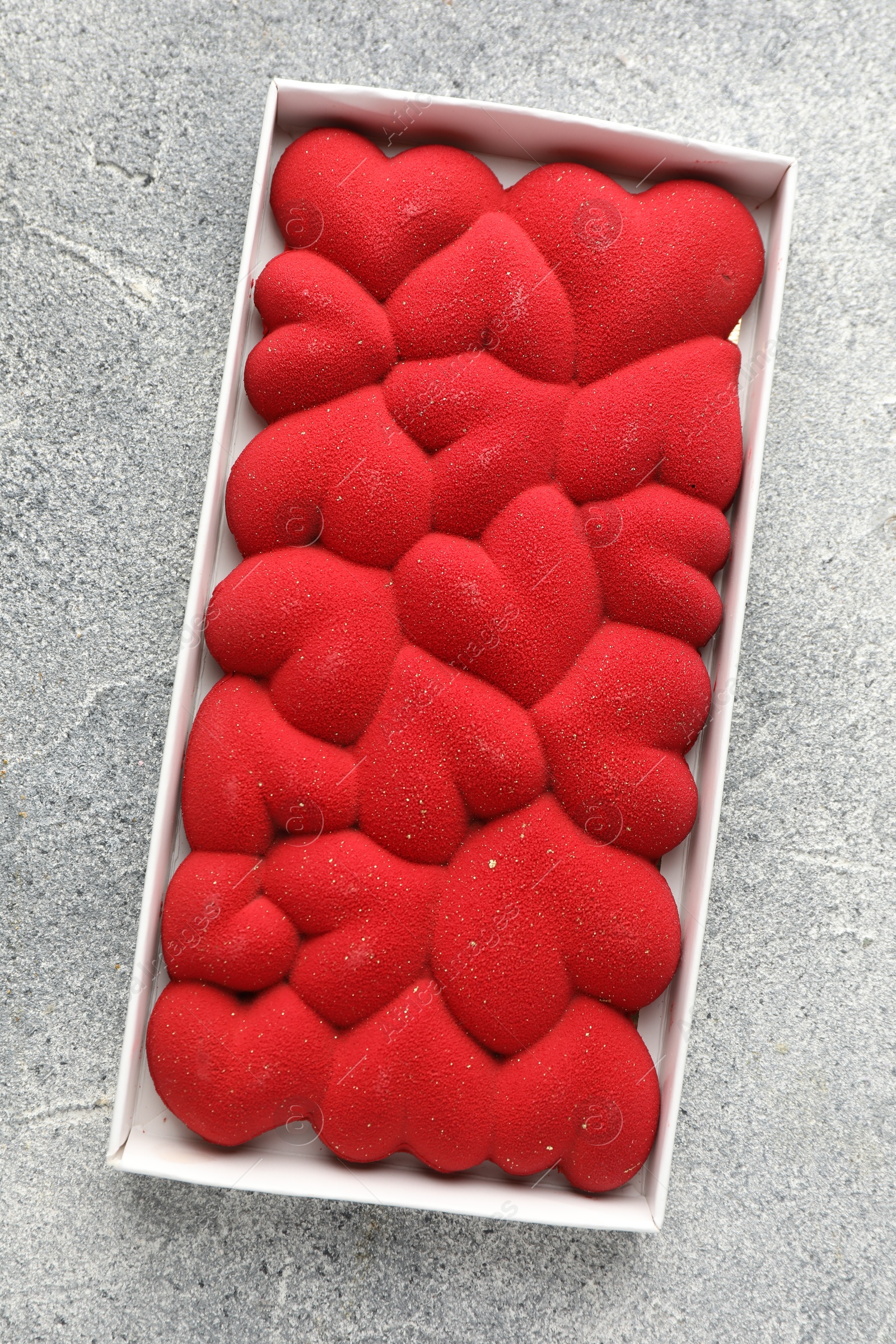 Photo of Chocolate bar decorated with hearts on grey textured background, top view