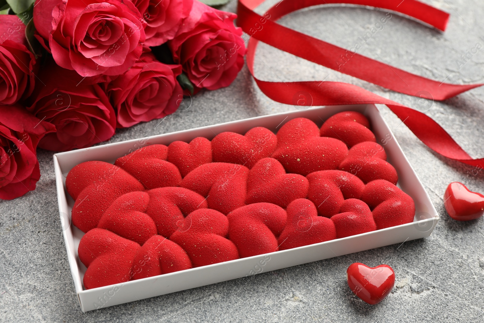 Photo of Chocolate bar decorated with hearts, candies, roses and ribbon on grey textured background, closeup