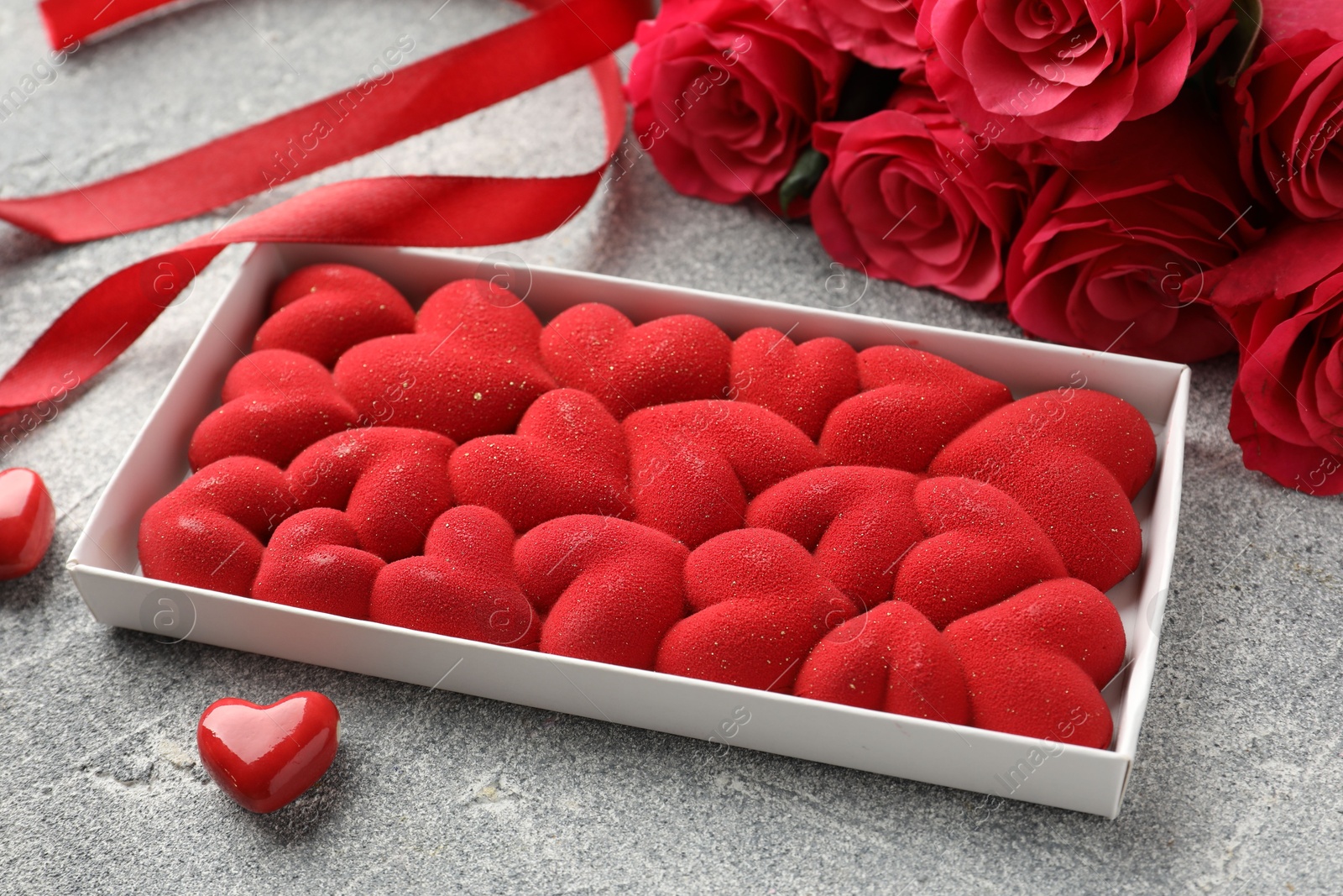 Photo of Chocolate bar decorated with hearts, candies, roses and ribbon on grey textured background, closeup