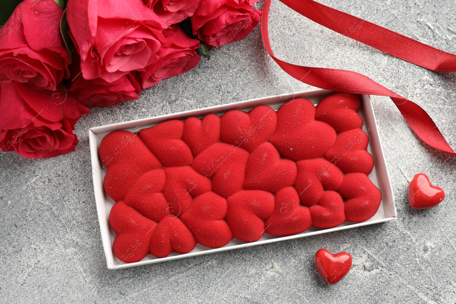 Photo of Chocolate bar decorated with hearts, candies, roses and ribbon on grey textured background, flat lay