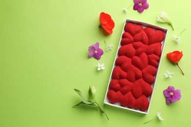 Photo of Chocolate bar decorated with hearts and flowers on green background, flat lay. Space for text