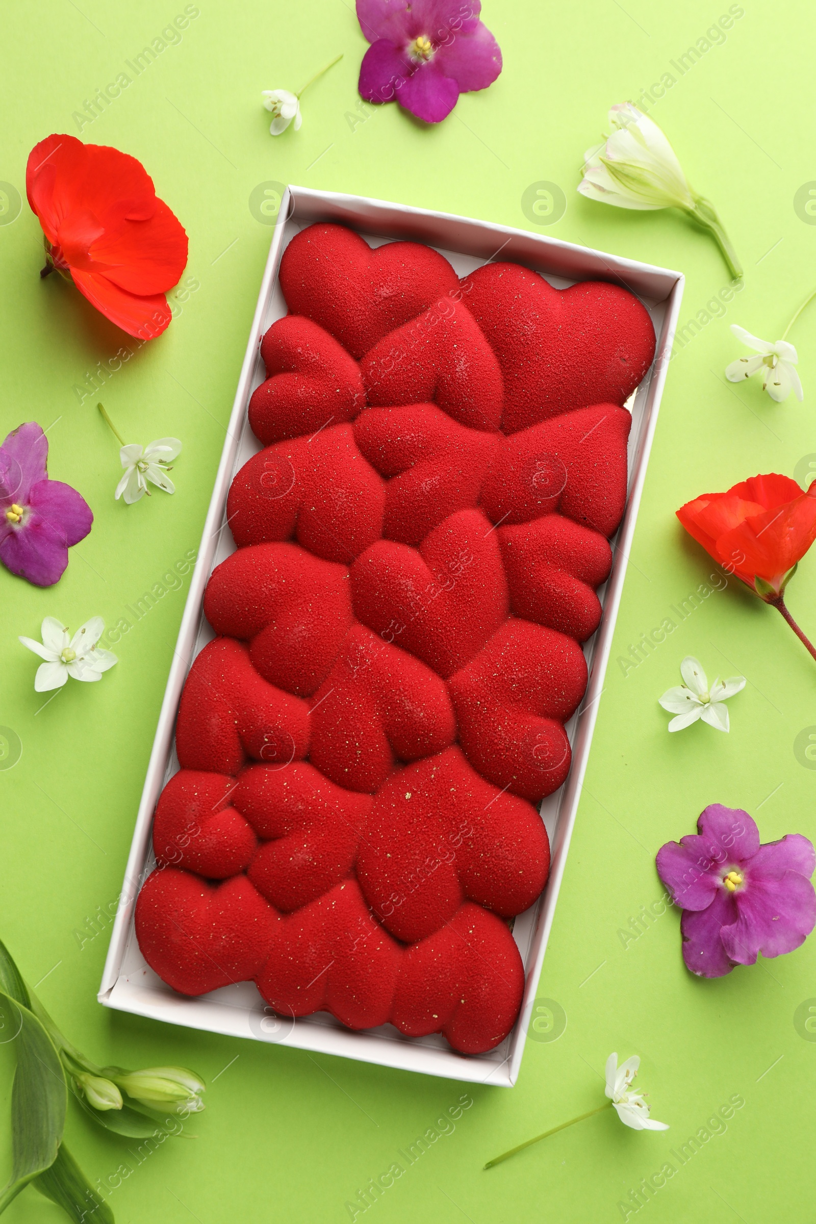 Photo of Chocolate bar decorated with hearts and flowers on green background, flat lay