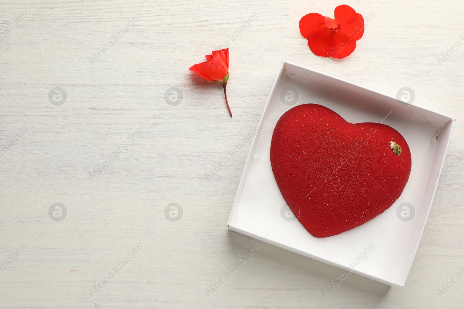 Photo of Heart shaped chocolate in box and flowers on light wooden background, top view. Space for text