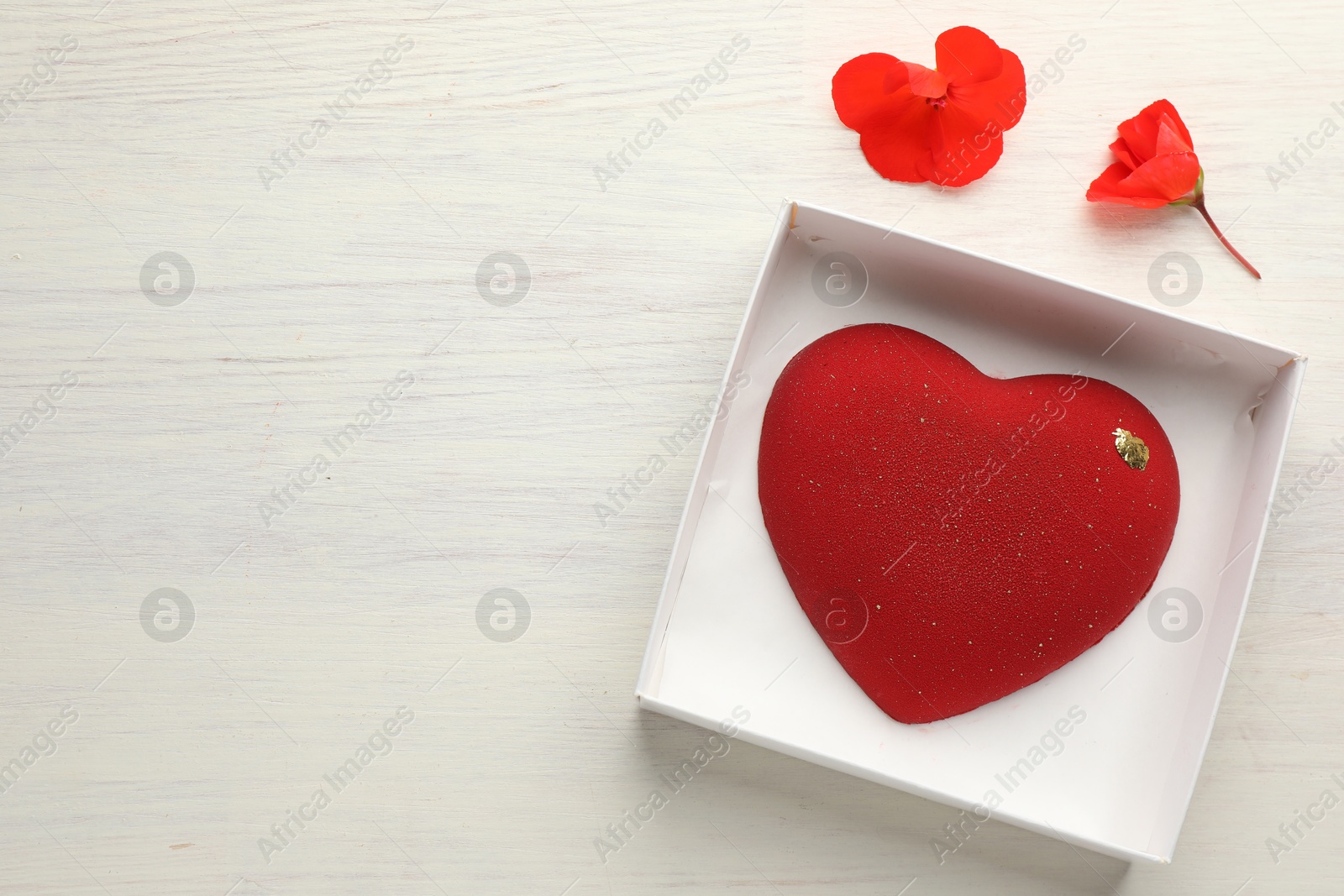 Photo of Heart shaped chocolate in box and flowers on light wooden background, top view. Space for text