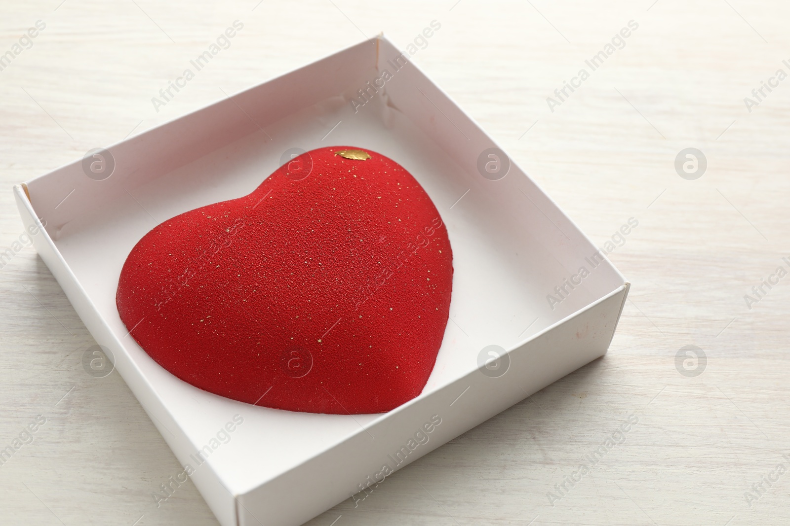 Photo of Heart shaped chocolate in box on light wooden background, closeup