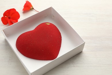 Photo of Heart shaped chocolate in box and flowers on light wooden background, closeup