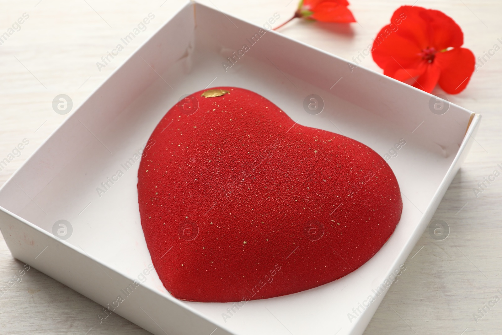 Photo of Heart shaped chocolate in box and flowers on light wooden background, closeup