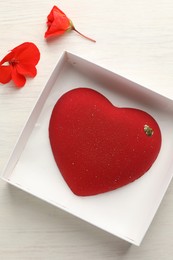 Photo of Heart shaped chocolate in box and flowers on light wooden background, top view