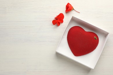 Photo of Heart shaped chocolate in box and flowers on light wooden background, top view. Space for text