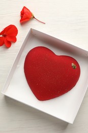 Photo of Heart shaped chocolate in box and flowers on light wooden background, top view