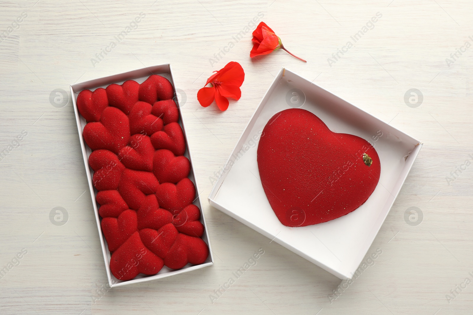 Photo of Heart shaped chocolates and flowers on light wooden background, top view