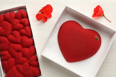 Photo of Heart shaped chocolates and flowers on light wooden background, top view