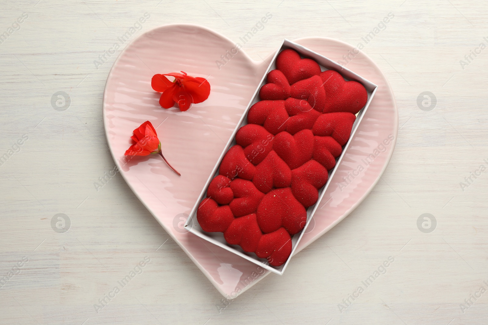 Photo of Chocolate bar decorated with hearts and flowers on light wooden background, top view