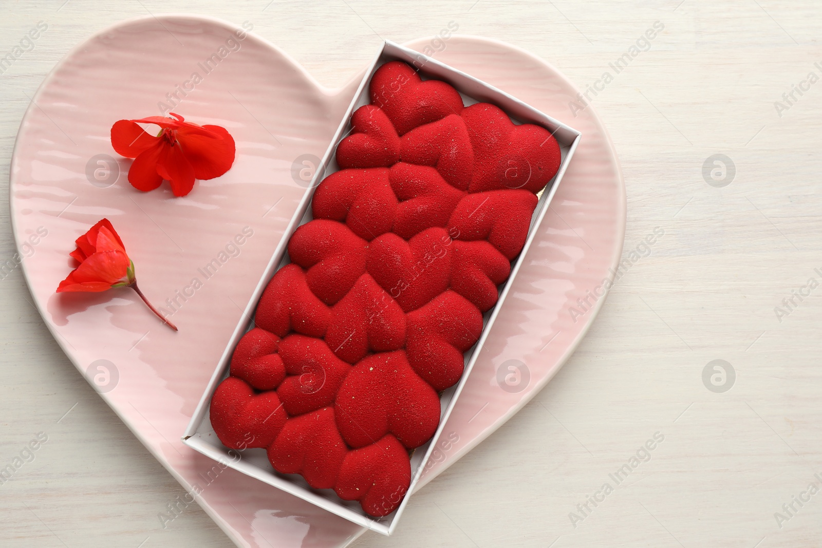 Photo of Chocolate bar decorated with hearts and flowers on light wooden background, top view