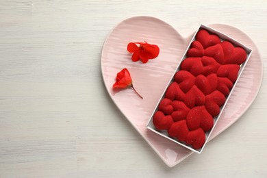 Photo of Chocolate bar decorated with hearts and flowers on light wooden background, top view. Space for text