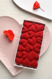 Photo of Chocolate bar decorated with hearts and flowers on light wooden background, top view