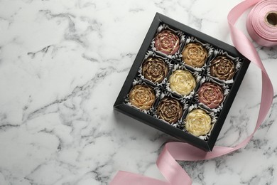 Photo of Delicious flower shaped chocolate bonbons in box and ribbon on white marble background, top view. Space for text