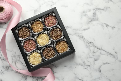 Photo of Delicious flower shaped chocolate bonbons in box and ribbon on white marble background, top view. Space for text