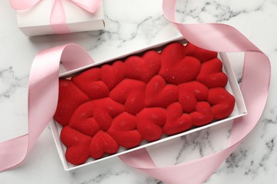 Photo of Chocolate bar decorated with hearts and ribbon on white marble background, top view