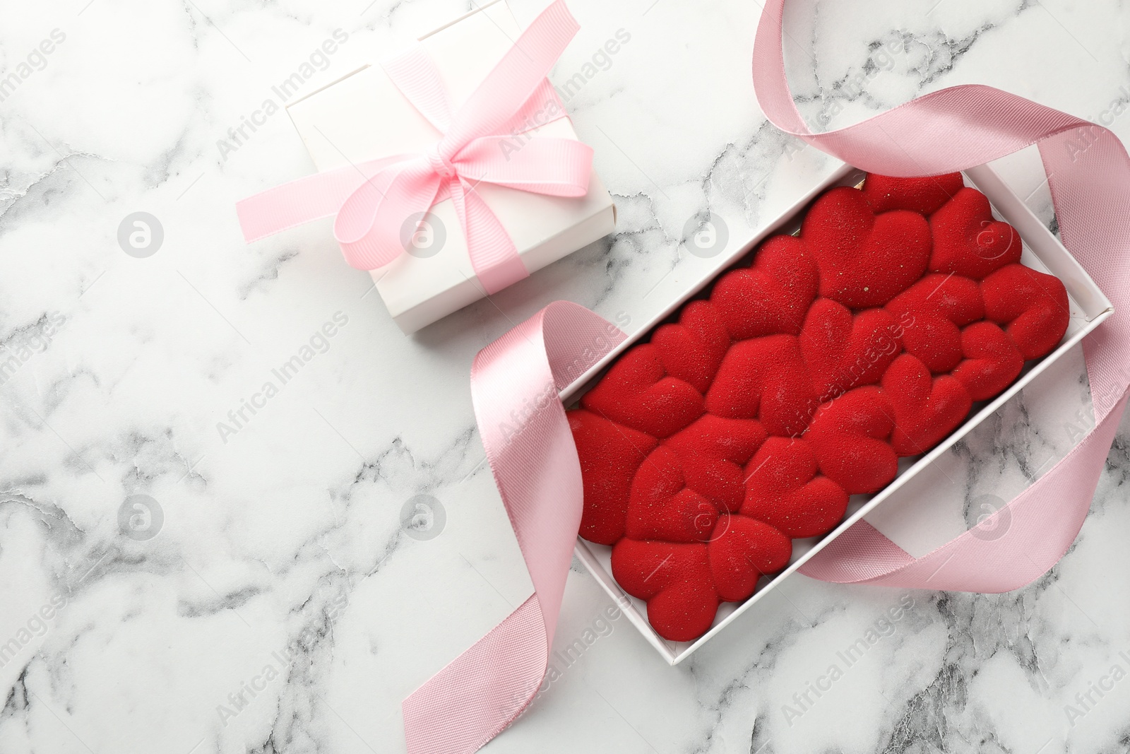 Photo of Chocolate bar decorated with hearts and ribbon on white marble background, top view. Space for text