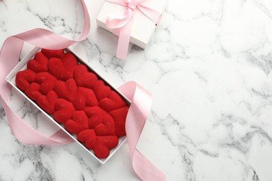 Photo of Chocolate bar decorated with hearts and ribbon on white marble background, top view. Space for text