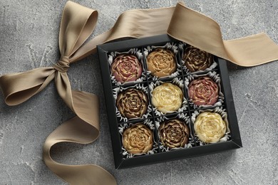 Photo of Delicious flower shaped chocolate bonbons in box and bow on grey textured background, top view