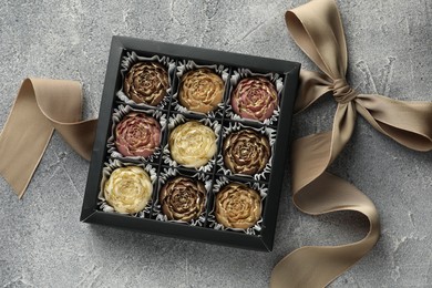 Photo of Delicious flower shaped chocolate bonbons in box and bow on grey textured background, top view