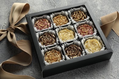 Photo of Delicious flower shaped chocolate bonbons in box and bow on grey textured background, closeup